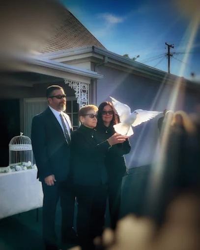 Grieving family in black at a memorial service as a woman releases a white dove beside a white birdcage
